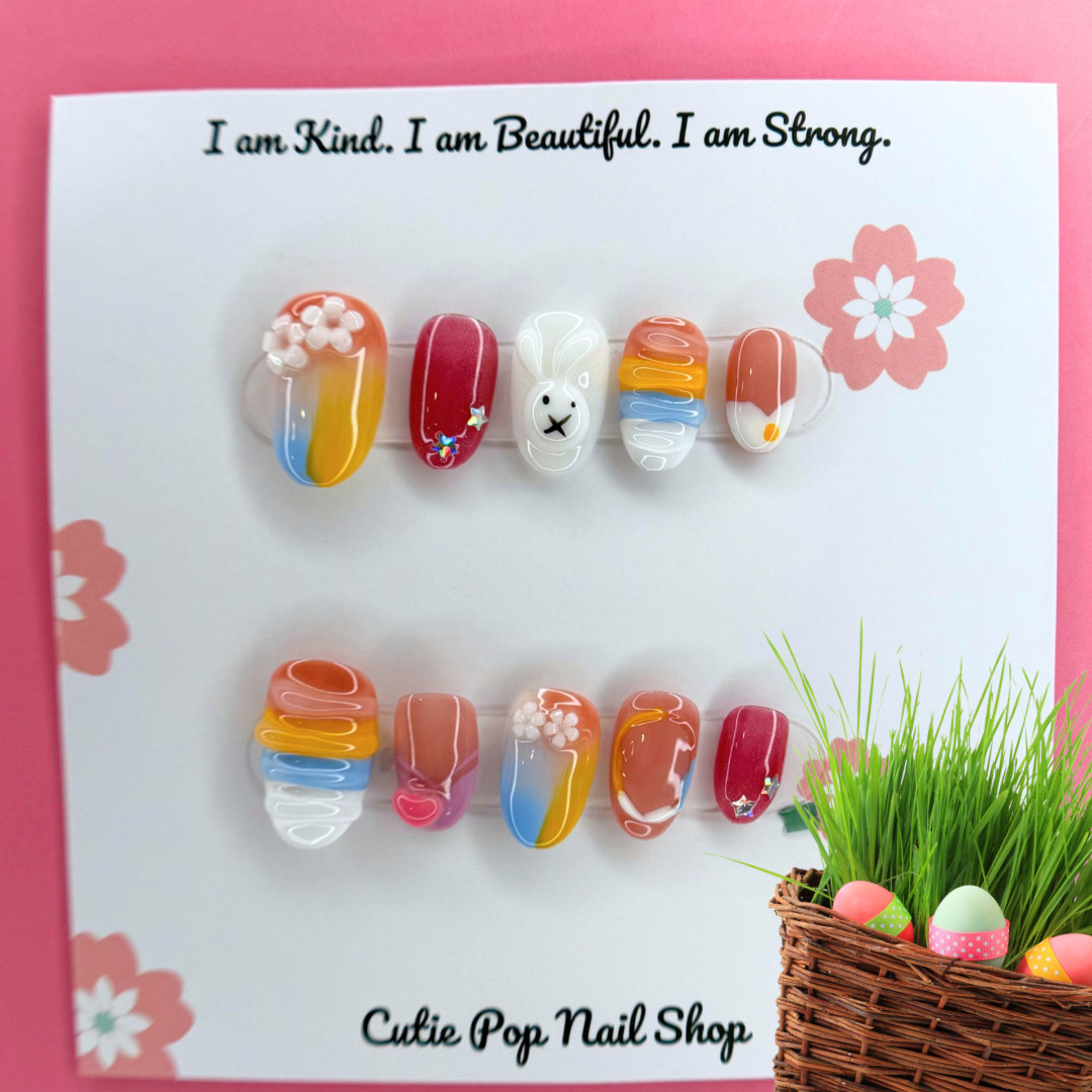 Kawaii Bunny Pastel Rainbow press-on nails by CutiePop Nail Shop featuring medium-length round/oval nails in a mix of soft pastel hues—baby pink, lavender, mint green, and pale yellow—with whimsical hand-painted bunny faces, cloud and rainbow motifs, heart and star accents over a dreamy gradient. Comes as a full DIY-ready kit including ten reusable handmade nails, jelly adhesive tabs, a mini nail file, and a cuticle stick—perfect for a bright, cute-and-playful kawaii-inspired manicure.