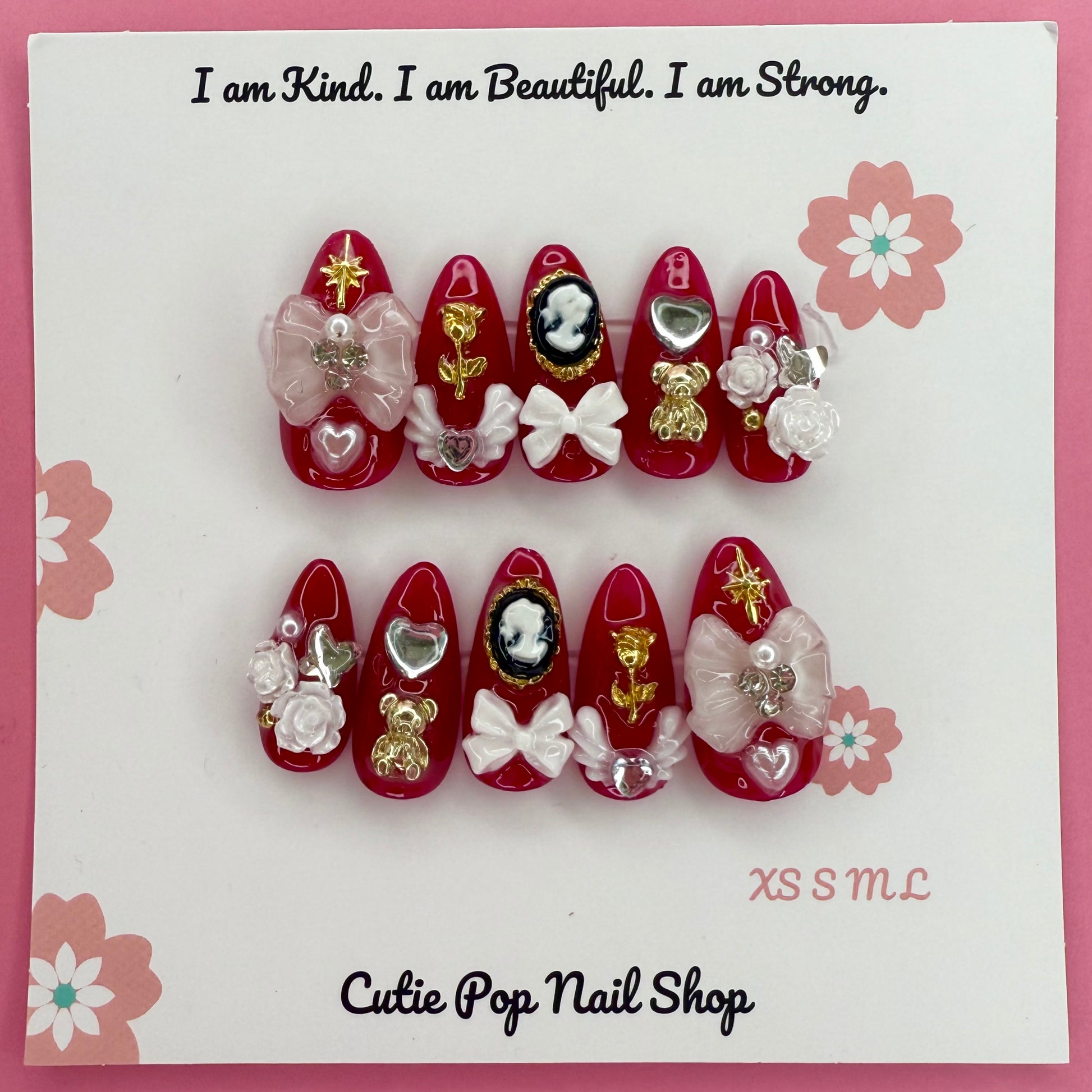 Victorian Shadows – Red press on nails by CutiePop Nail Shop featuring medium almond shaped nails in a deep red tone, adorned with delicate white rose art and ribbon details for a romantic gothic look.