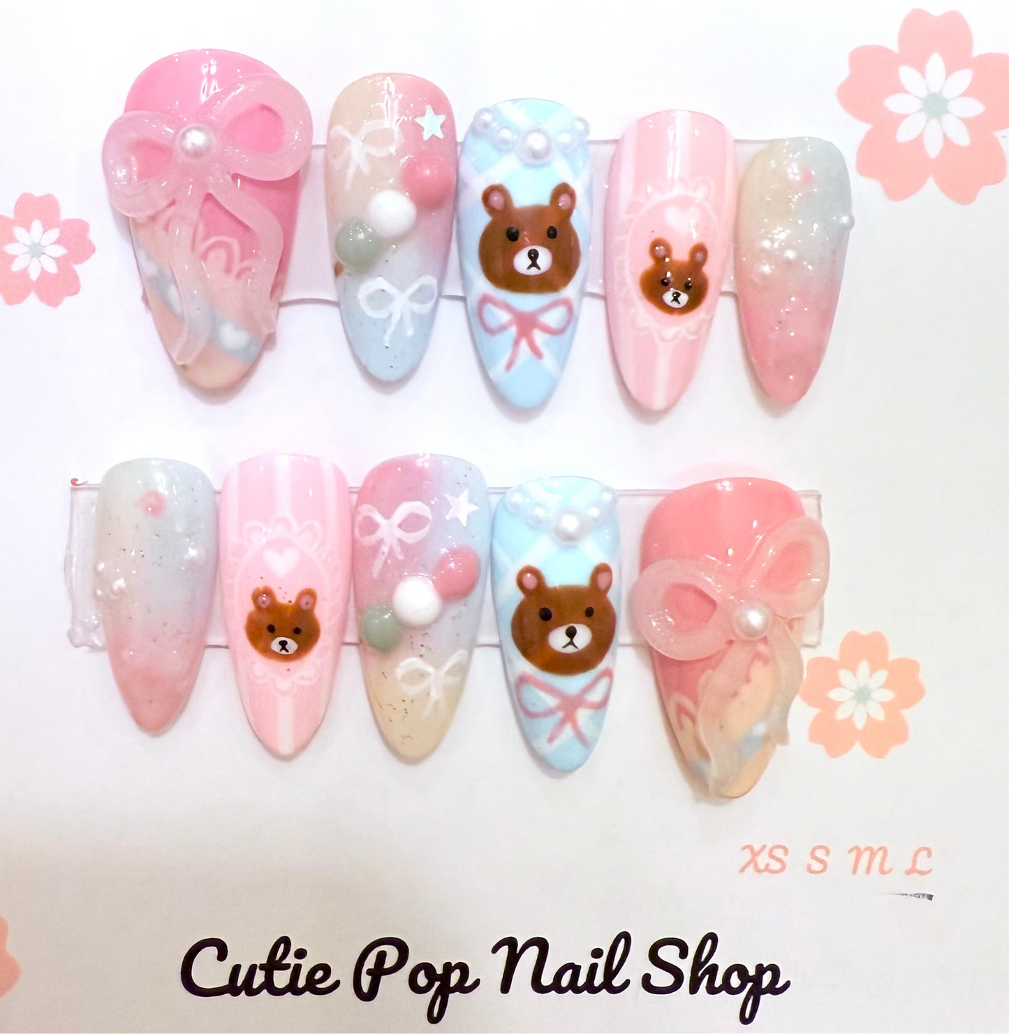 Dango Bear press-on nails by CutiePop Nail Shop featuring medium-length almond-shaped nails in pastel pink and light blue tones. Accented with subtle rainbow shimmer, pearl details, ribbon charms, and an adorable bear design for a sweet and playful kawaii look.