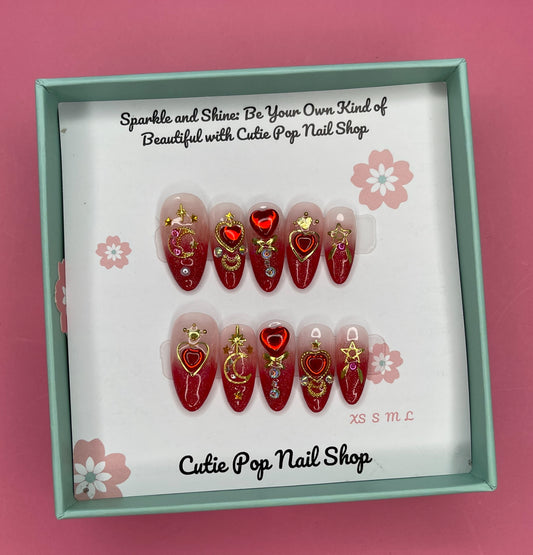 Cosmic Moon – Mars I press on nails by CutiePop Nail Shop featuring medium almond shaped nails in bold red and soft white tones, adorned with gold heart and crescent moon charms for a dreamy, cosmic look inspired by Sailor Mars.