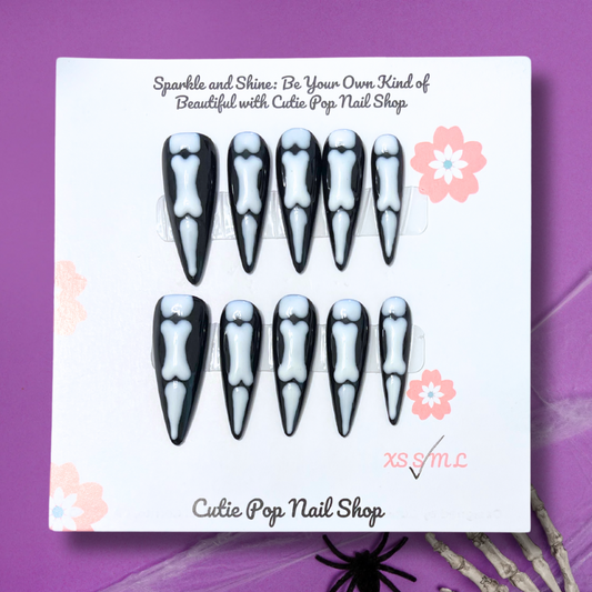Bones Halloween Nails by CutiePop Nail Shop featuring stiletto shaped nails in bold black and white tones with skeleton and bone designs—perfect for a spooky yet stylish Halloween look.