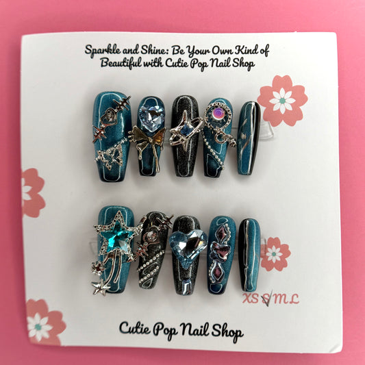 Y2K Teal Silver press on nails by CutiePop Nail Shop featuring medium coffin shaped nails in bold teal and silver tones with a chrome finish, heart and star accents, and a rock star-inspired Y2K aesthetic.