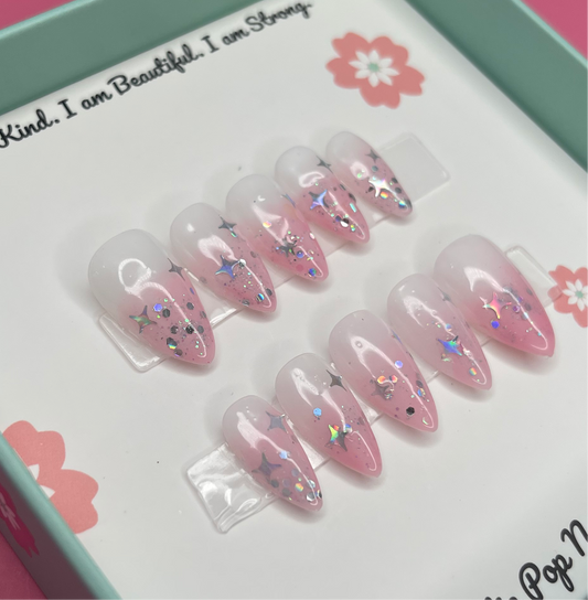 Fantasy (Blush Pink) press‑on nails by CutiePop Nail Shop featuring short to medium-length almond-shaped nails with a dreamy blush‑pink syrup jelly gel polish. The sheer gradient finish reflects light like a soft glow, creating an ethereal, fantasy-inspired aesthetic. Includes a reusable kit with ten handmade nails, jelly adhesive tabs, a mini nail file, and a cuticle stick—perfect for a subtle, enchanting manicure.