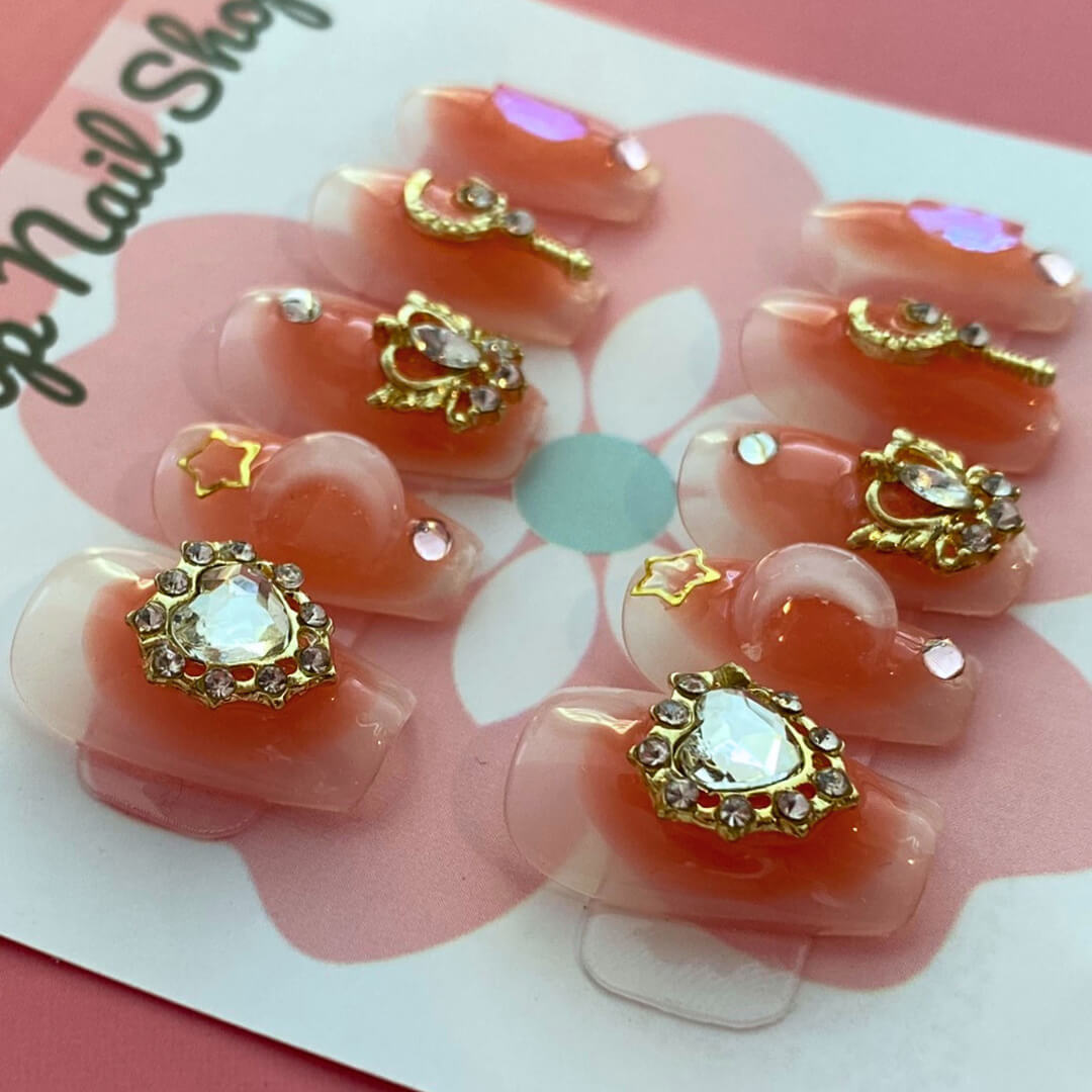 Blushing Moon press-on nails by CutiePop Nail Shop feature medium-length coffin-shaped nails in a blush-pink base, adorned with oversized starburst gem clusters, fine metallic glitter, and soft pearlescent shimmer. This dreamy set creates a romantic, glamorous statement look. Each kit includes 10 reusable handmade nails, jelly adhesive tabs, a mini nail file, and a cuticle stick for easy DIY application.