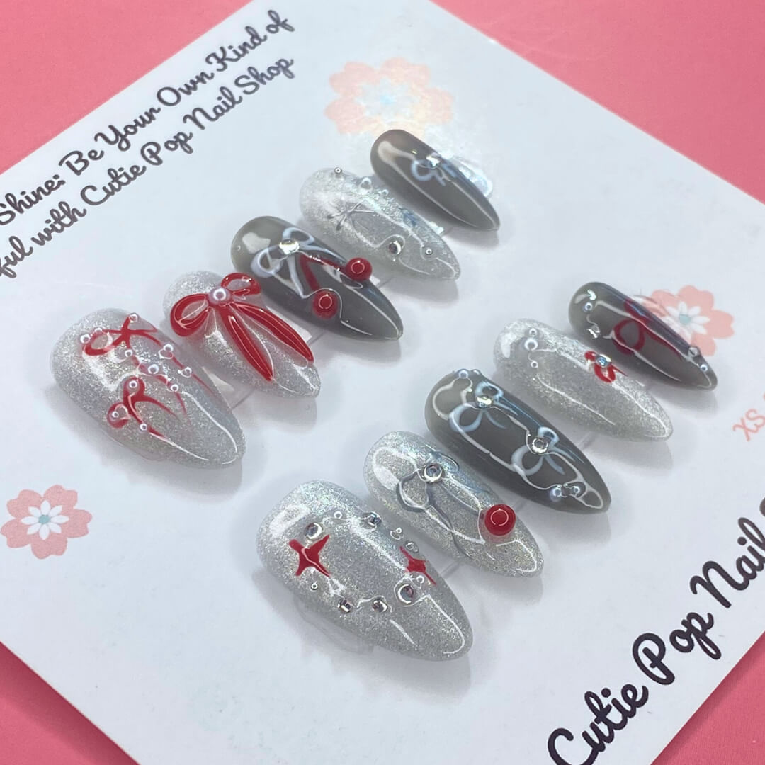 Bowtique Sparkle press‑on nails by CutiePop Nail Shop featuring a medium‑length almond‑shaped set coated in vibrant rose‑pink glitter polish, accented with dainty 3D bow-shaped charms and sparkling rhinestones, giving a flirty, playful yet glamorous aesthetic.