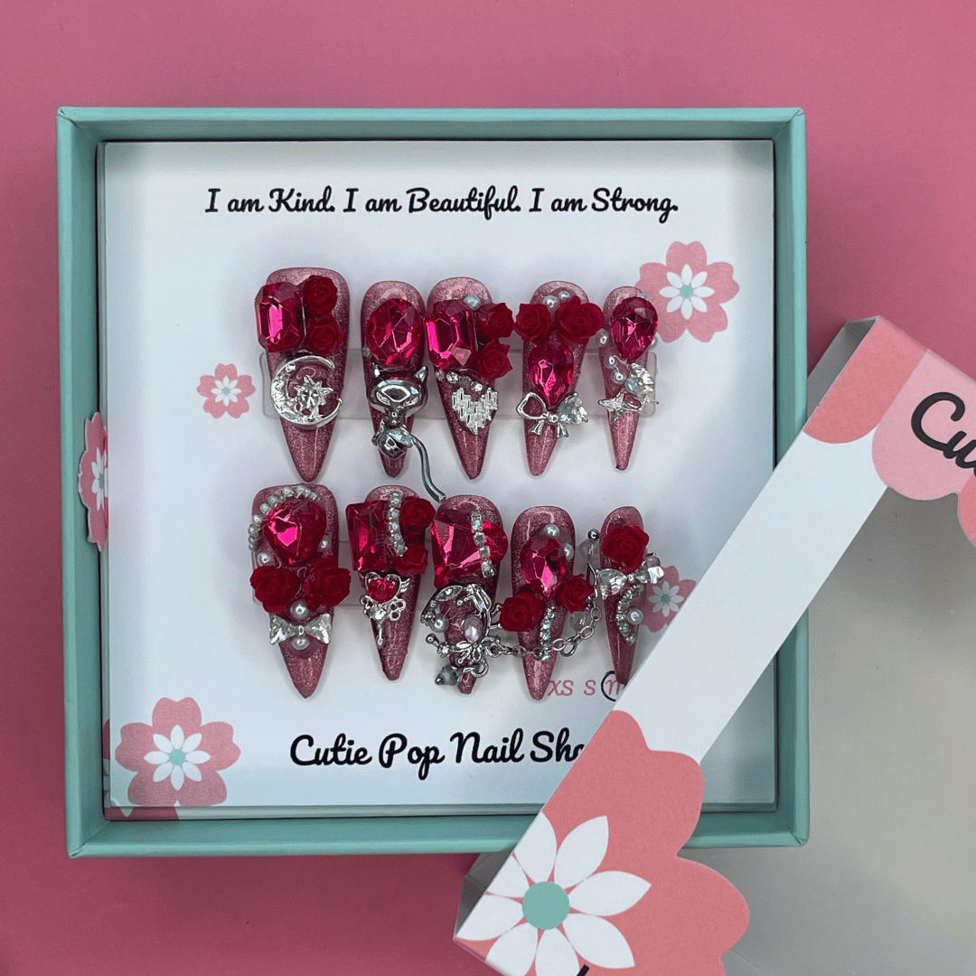Bougie Bling 11 press on nails by CutiePop Nail Shop featuring long stiletto shaped nails with a bold wine red glitter base layered with luxurious oversized 3D gem clusters in deep jewel tones, accented with sparkling rhinestones and metallic detailing. Hand sculpted for a dramatic, upscale statement mani.