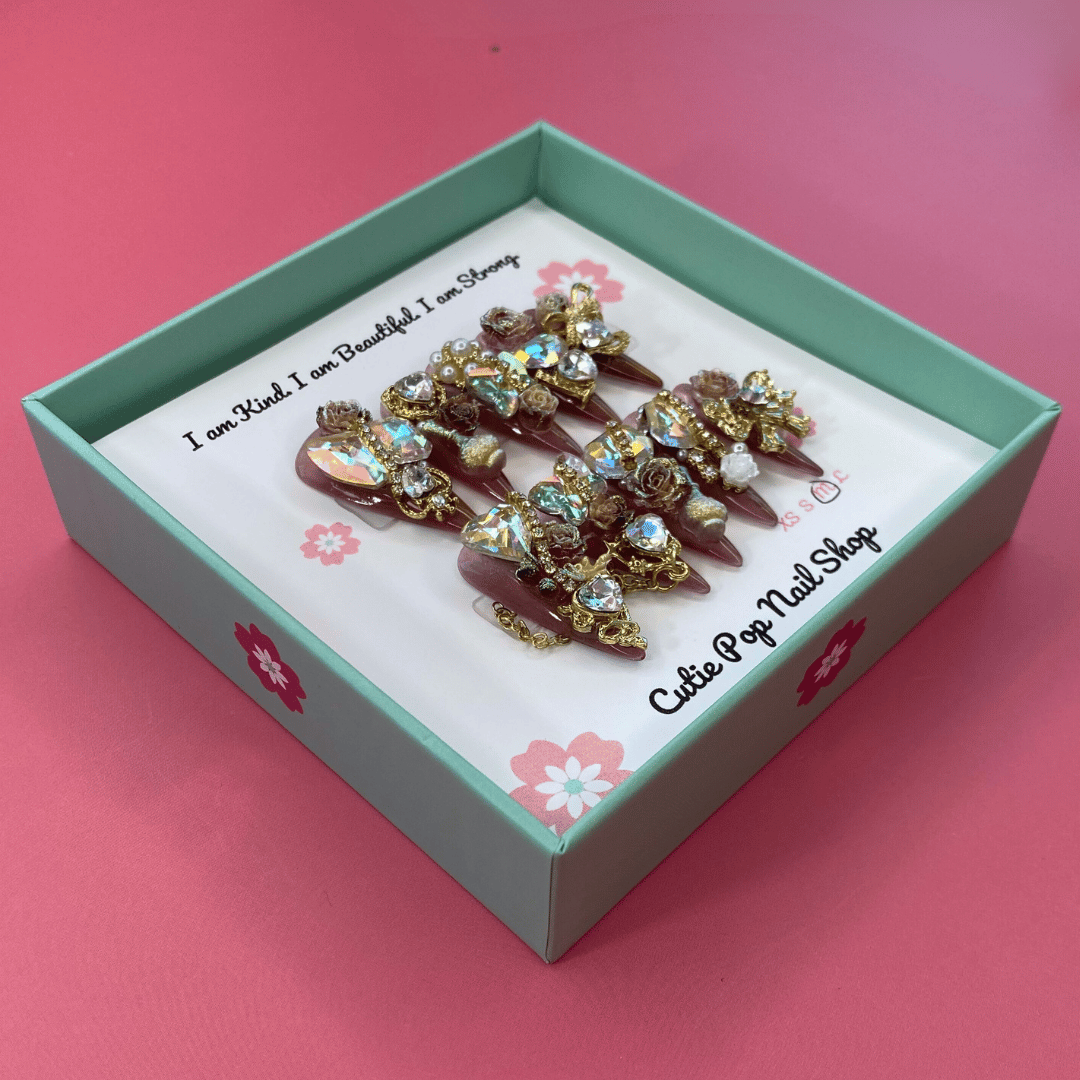 Bougie Bling 12 press on nails by CutiePop Nail Shop featuring long stiletto shaped nails with a glamorous deep dark burgundy or smoky wine toned glitter base. Lavish oversized 3D gem clusters in jewel tones such as ruby and crystal are complemented by sparkling rhinestones and metallic accents—arranged in an opulent, high impact luxury statement manicure.