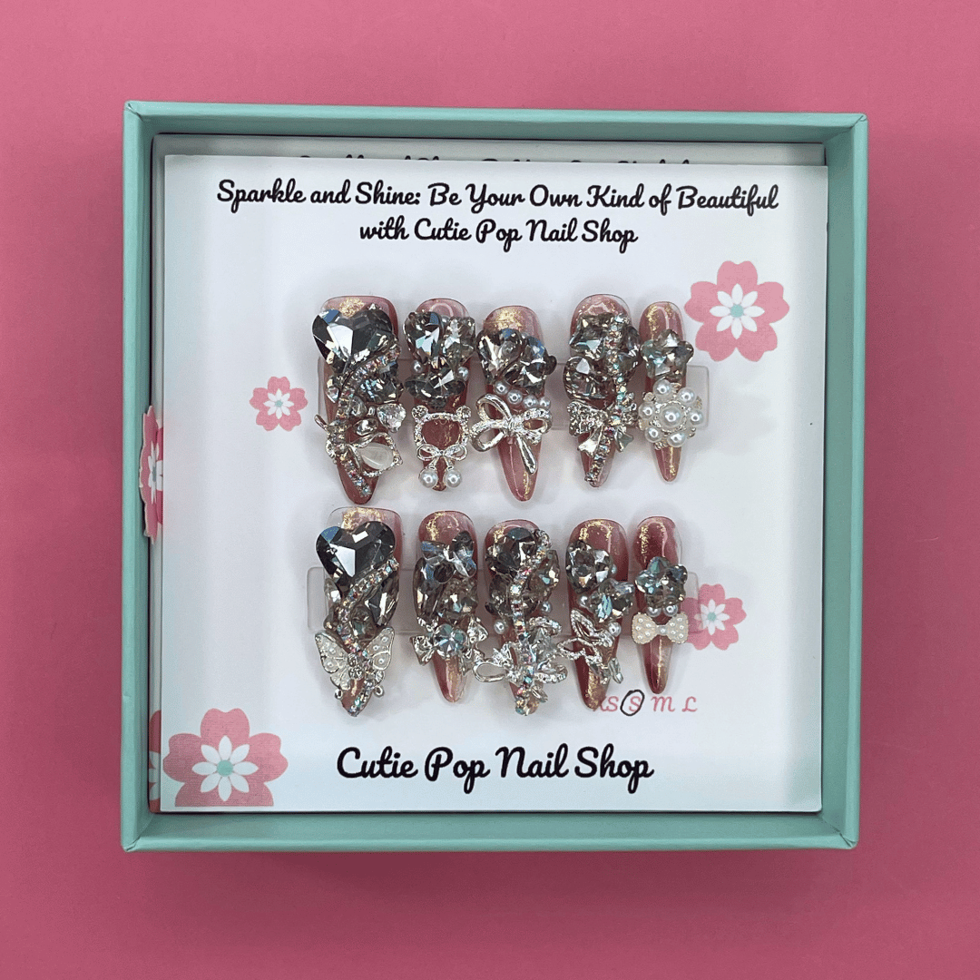 Bougie Bling 14 press on nails by CutiePop Nail Shop featuring long stiletto shaped nails with a dramatic glossy black base adorned with sparkling silver glitter accents and glamorous oversized 3D gem clusters in clear, smoke, and metallic tones, meticulously arranged for a bold, luxurious statement manicure.
