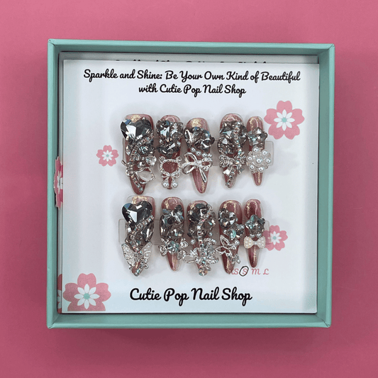Bougie Bling 14 press on nails by CutiePop Nail Shop featuring long stiletto shaped nails with a dramatic glossy black base adorned with sparkling silver glitter accents and glamorous oversized 3D gem clusters in clear, smoke, and metallic tones, meticulously arranged for a bold, luxurious statement manicure.