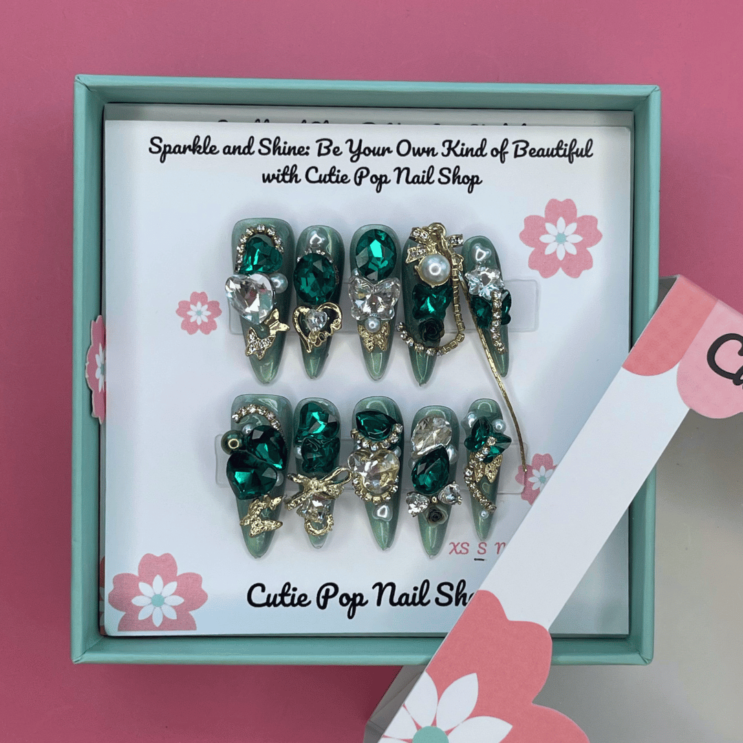 Bougie Bling 15 press on nails by CutiePop Nail Shop showcasing long coffin shaped nails with a dramatic glittery black base embellished with oversized 3D gem clusters in jewel tones, delicate rhinestone accents, and metallic detailing—all arranged in an ornate, high-impact luxury statement manicure.