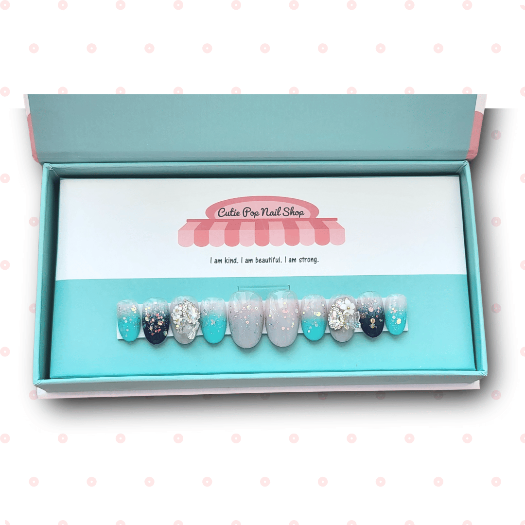 Fairytale press‑on nails by CutiePop Nail Shop featuring medium-length almond and round-shaped nails in a dreamy turquoise-to-navy gradient. These whimsical nails are accented with iridescent resin butterfly charms, holographic sequin glitter, and shimmering tones that evoke a magical wonderland vibe. Each set includes 10 reusable handmade nails, jelly adhesive tabs, a mini nail file, and a cuticle stick—perfect for an elegant yet playful fairy-tale inspired manicure.