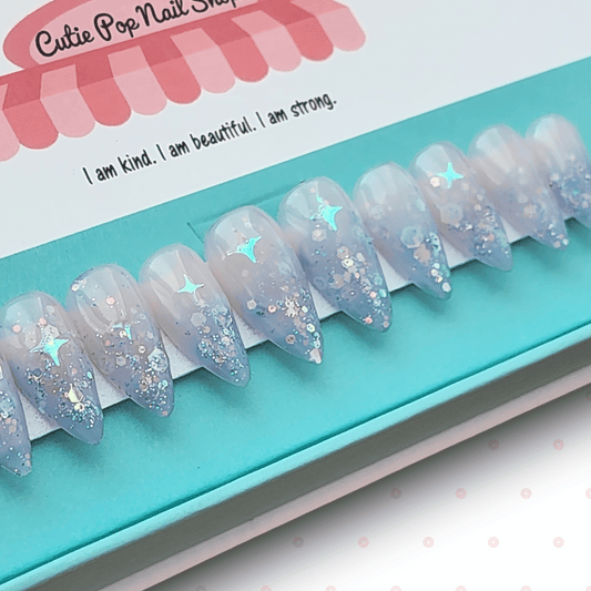 Fantasy (Lavender) press‑on nails by CutiePop Nail Shop featuring short-to-medium length almond-, round-, or coffin-shaped nails coated in dreamy lavender syrup jelly gel polish. Each nail is sprinkled with holographic star sequin glitter for a celestial shimmer effect. The set includes ten handmade reusable nails, jelly adhesive tabs, a mini nail file, and a cuticle stick—offering a whimsical, fantasy-inspired manicure perfect for summer enchantment.