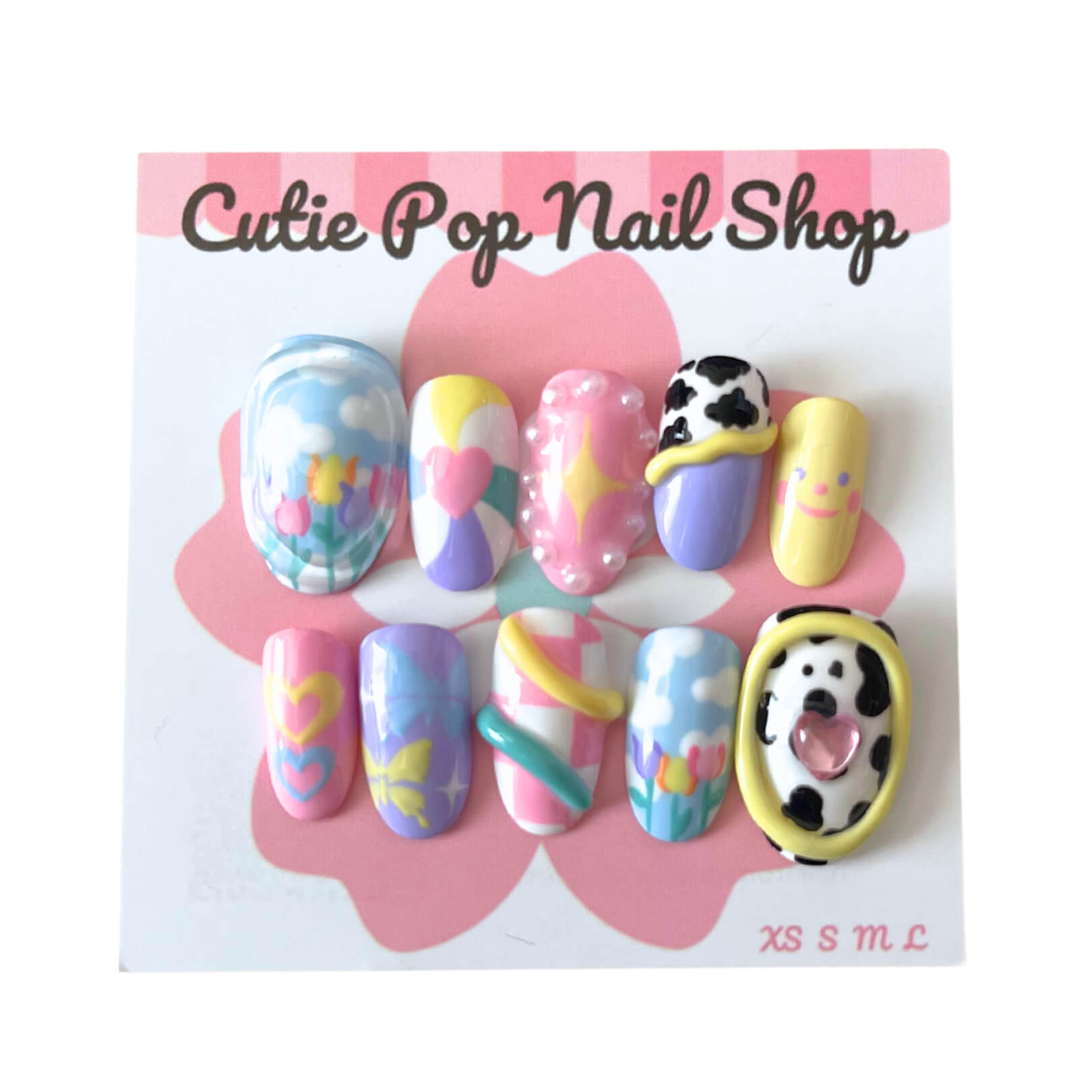 Dreamy Pastel press‑on nails by CutiePop Nail Shop featuring short- to medium-length round nails in a playful blend of soft pastel tones—baby pink, mint, lavender, and pale yellow—adorned with hand-painted flowers, hearts, stars, and whimsical designs. Includes reusable adhesive tabs, mini nail file, and cuticle stick for a full kit experience, creating a charming, fanciful aesthetic.