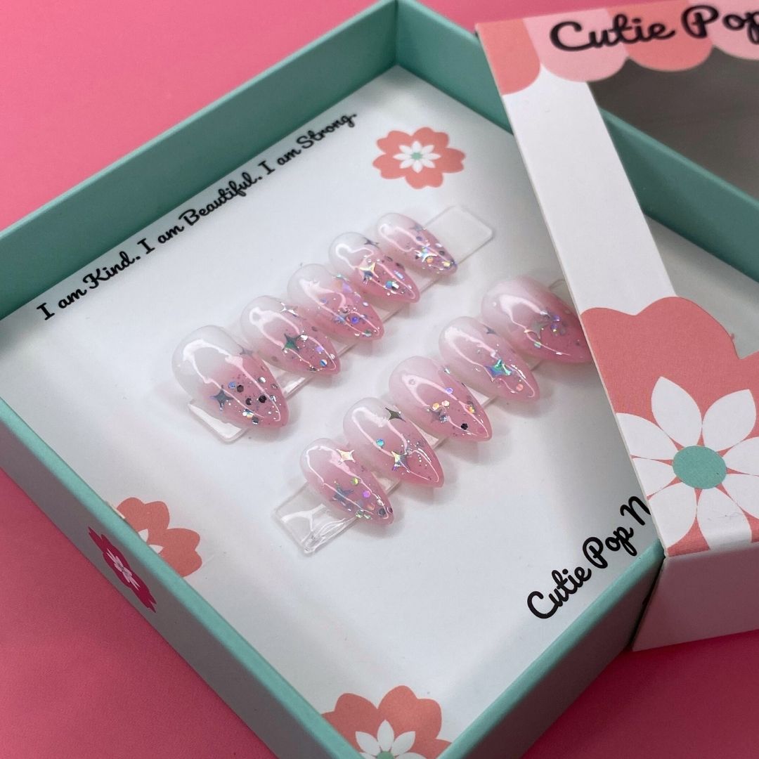 Fantasy (Blush) press-on nails by CutiePop Nail Shop featuring medium-length almond-shaped nails in soft blush pink tones. Designed with dreamy elements like pearls, subtle shimmer, and delicate accents, this set evokes a whimsical, fairy-like aesthetic. Comes with 10 reusable handmade nails, jelly adhesive tabs, a mini nail file, and a cuticle stick for easy at-home application.