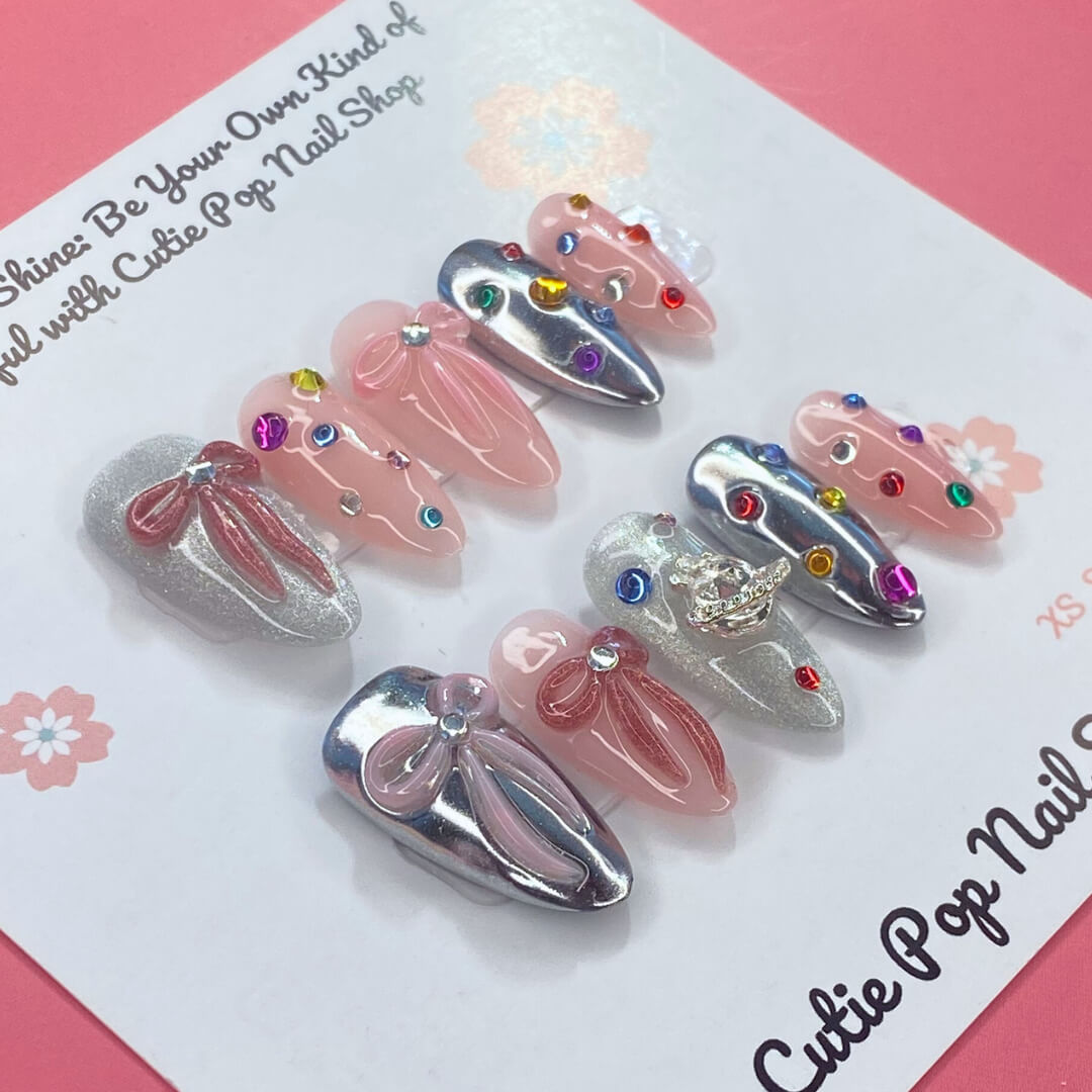 Gem Princess press-on nails by CutiePop Nail Shop featuring a creamy blush-pink base with ultra-fine shimmer, hand-placed pastel gem clusters, and clear rhinestones. Select nails are accented with tiny pearls or heart motifs for added charm. Crafted in a medium-length almond shape with a glossy gel finish, this design brings an elegant and whimsical princess-like aesthetic to your manicure. Each set includes 10 reusable handmade nails, jelly adhesive tabs, a mini nail file, and a cuticle stick for effortles