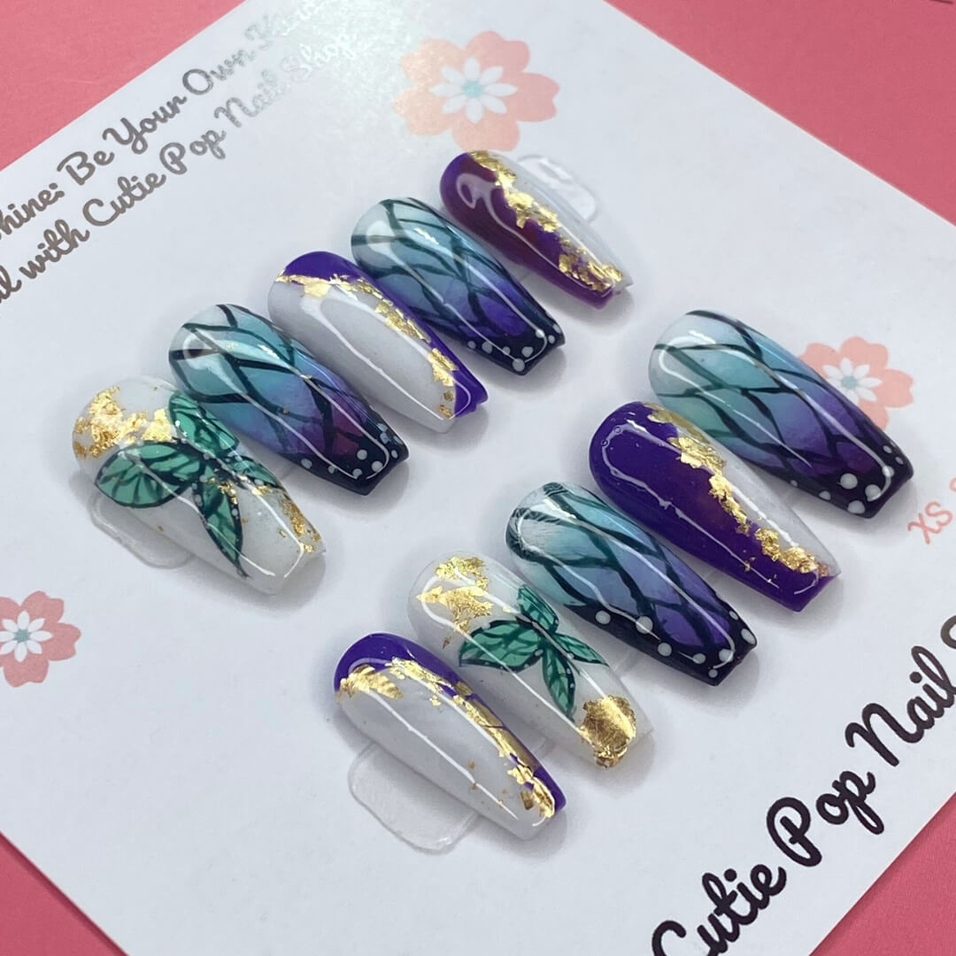 Shinobu Butterfly press on nails by CutiePop Nail Shop featuring medium coffin shaped nails in an elegant blend of soft lavender, mint, and pale pink tones. Hand painted butterfly wing patterns inspired by the Demon Slayer Insect Hashira are accented with fine glitter shimmer and delicate metallic veins. Finished with a glossy gel coat for a graceful, ethereal aesthetic.
