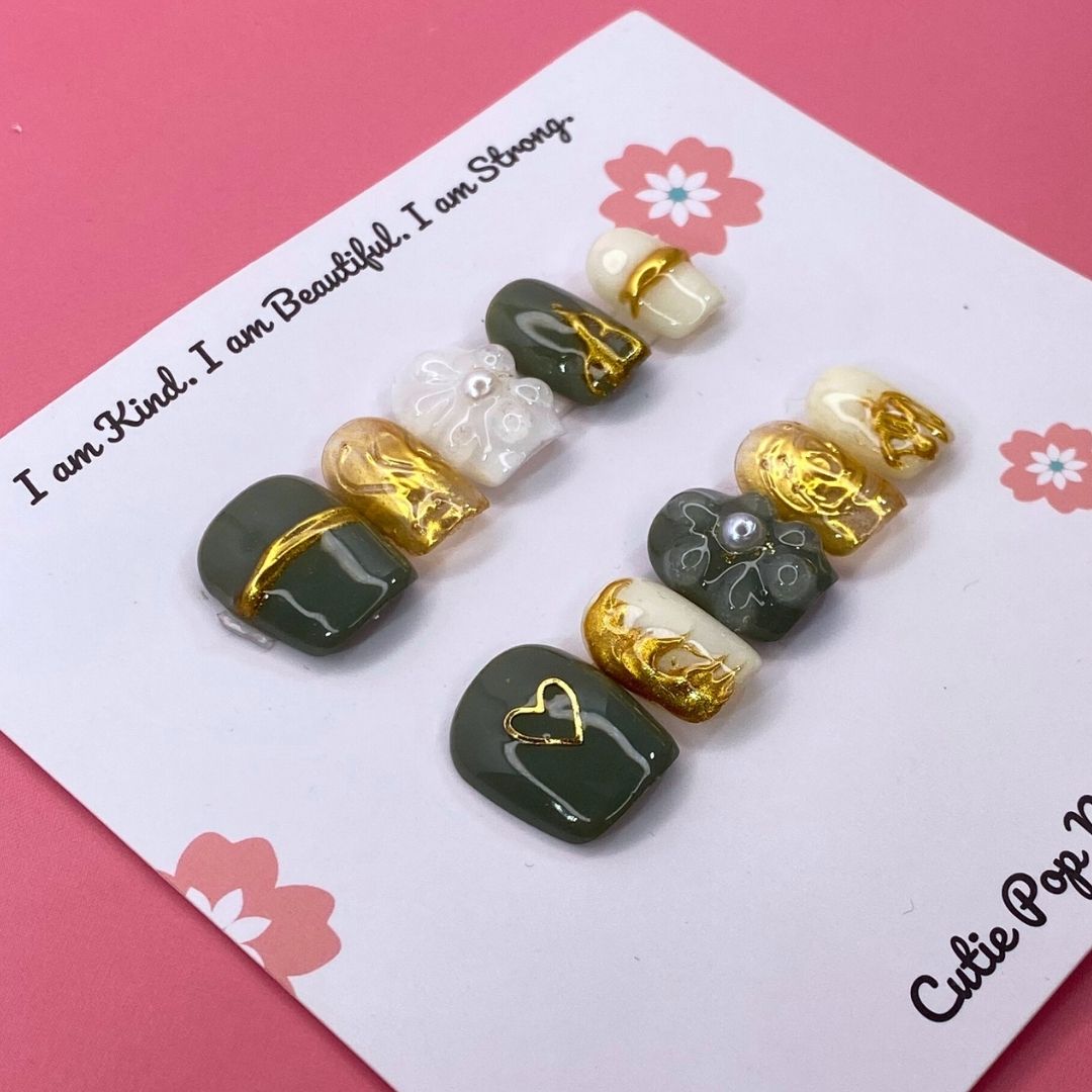 Golden Lady press-on nails by CutiePop Nail Shop featuring short squoval-shaped nails in elegant nude and gold tones, adorned with metallic accents and fine glitter for a luxurious, feminine finish.