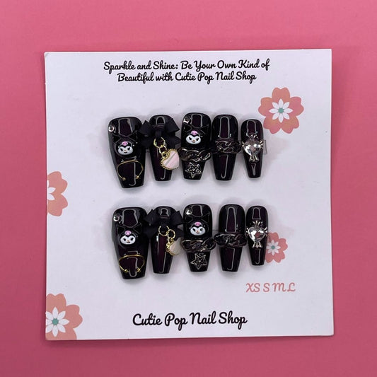 Kuromicore press on nails by CutiePop Nail Shop inspired by Kuromi, featuring medium coffin shaped nails in black and pink tones with cute gothic elements like hearts, skulls, and bows for a playful yet edgy look.