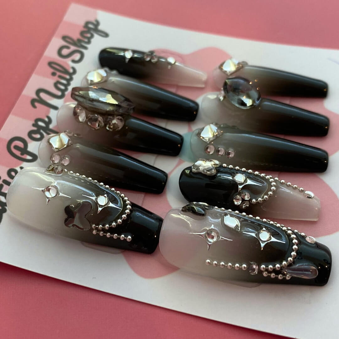 Midnight Whisper press-on nails by CutiePop Nail Shop featuring medium-length coffin-shaped nails with a deep black base, silvery metallic swirl motifs, and star-like shimmer accents. Designed in a limited-edition celestial gothic style, this set captures whispery galaxy vibes with an elegant, mysterious flair. Each kit includes 10 reusable handmade nails, jelly adhesive tabs, a mini nail file, and a cuticle stick for easy DIY application.