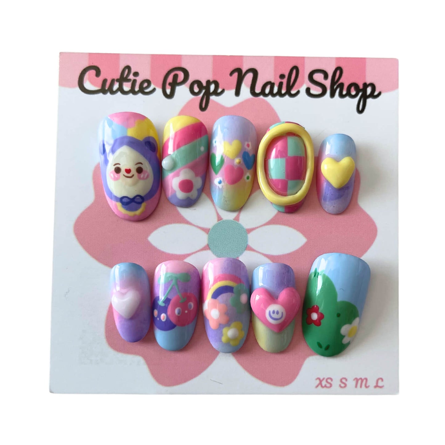 Pastal Friends press‑on nails by CutiePop Nail Shop showcasing a fun round-shaped, short-length set in soft pastel hues—featuring hand-painted cherries, charming hearts, cheerful flowers, and a cute doll motif on alternating nails. Includes the full reusable kit with adhesive tabs, mini file, and cuticle stick for a whimsical, kawaii‑inspired look.