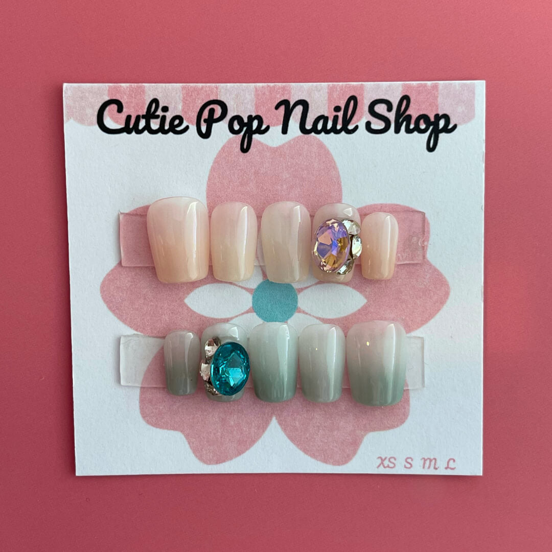 Pastel Gem press‑on nails by CutiePop Nail Shop featuring short, square-shaped nails in soft pastel hues—including blush pinks, mint green, and lavender—adorned with oversized iridescent gem embellishments and subtle metallic accents. Includes a reusable set with adhesive tabs, a mini nail file, and a cuticle stick, offering a sweet, dreamy manicure with a touch of luxe sparkle.