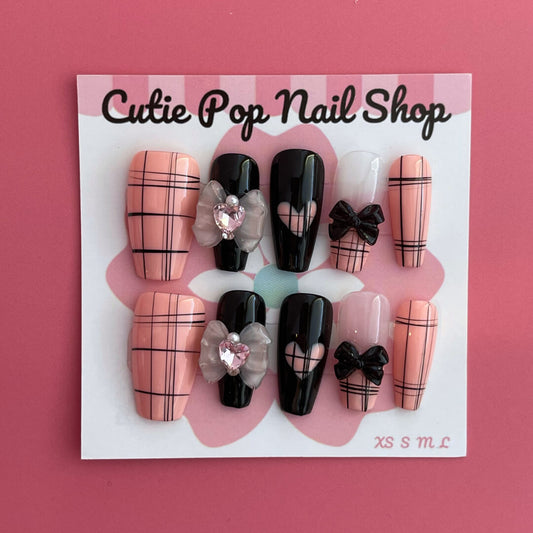 Pink Loli press on nails by CutiePop Nail Shop featuring a playful mix of pink based nails with edgy black line detailing and black accent nails adorned with ribbon, butterfly-like shapes, and heart motifs. Designed in a coffin shape, this set blends sweet and dark elements for a bold, kawaii-meets-gothic aesthetic.