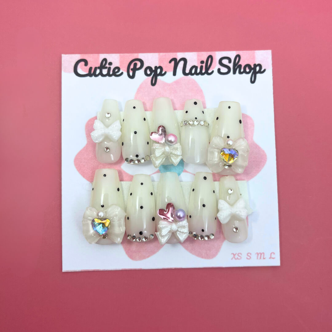 Polka Dot Pink press‑on nails by CutiePop Nail Shop featuring medium‑length coffin-shaped nails in a vibrant bubblegum-pink base with crisp white polka dots evenly spaced across each nail. The glossy finish enhances the playful, retro aesthetic. Includes a full reusable kit with ten handmade nails, jelly adhesive tabs, a mini nail file, and a cuticle stick—perfect for a fun, vintage-inspired manicure.