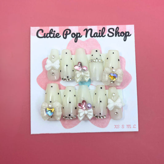 Polka Dot Pink press‑on nails by CutiePop Nail Shop featuring medium‑length coffin-shaped nails in a vibrant bubblegum-pink base with crisp white polka dots evenly spaced across each nail. The glossy finish enhances the playful, retro aesthetic. Includes a full reusable kit with ten handmade nails, jelly adhesive tabs, a mini nail file, and a cuticle stick—perfect for a fun, vintage-inspired manicure.