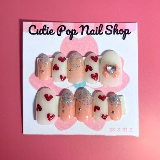 Red Hearts press-on nails by CutiePop Nail Shop featuring medium-length round-shaped nails in a bold red hue, adorned with charming red heart accents for a sweet, romantic look—perfect for Valentine’s vibes or year-round love.