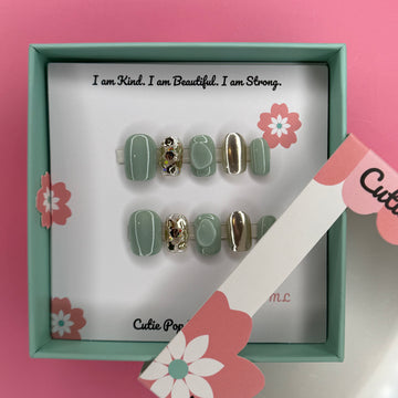 Green and Gold Sparkle press-on nails in a rich green base with sparkling gold accents and 3D bump embellishments, finished with a glossy shine – displayed on a Cutie Pop Nail Shop card.