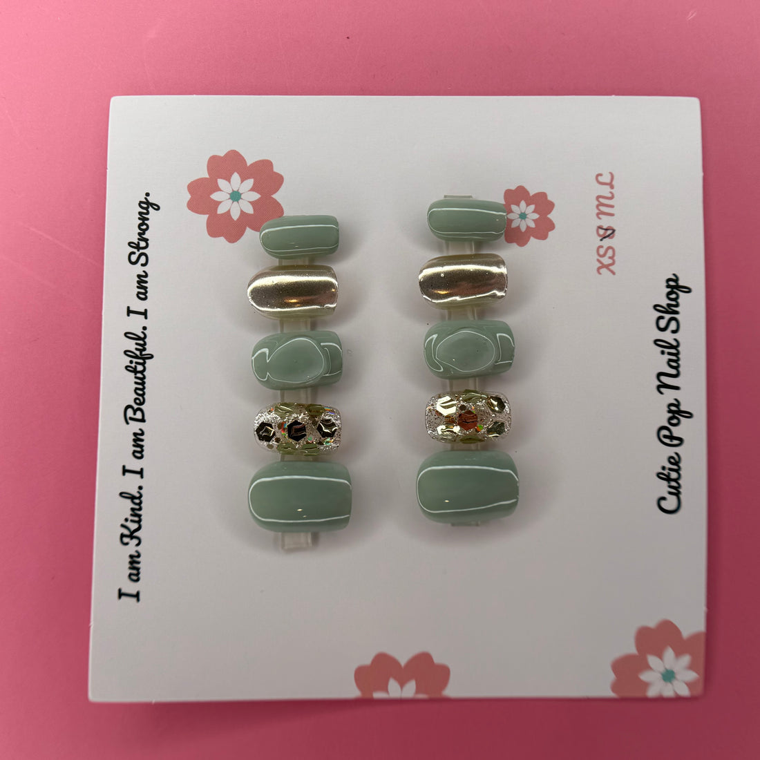Green and Gold Sparkle press-on nails in a rich green base with sparkling gold accents and 3D bump embellishments, finished with a glossy shine – displayed on a Cutie Pop Nail Shop card.