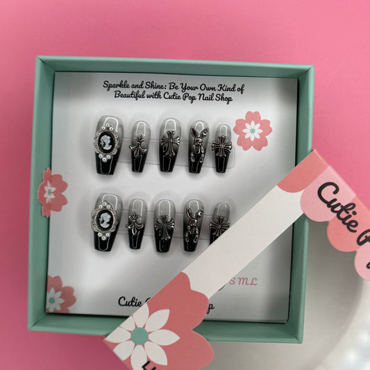Victorian Ombre press-on nails in a black and silver ombré design with glossy finish, featuring detailed 3D ornaments like a cross, bunny, and decorative charms – displayed on a Cutie Pop Nail Shop card.