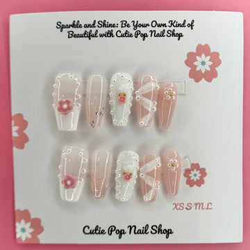 White Ribbon Pink Flower press-on nails by CutiePop Nail Shop featuring medium-length coffin-shaped nails in soft pink tones. Embellished with pearl accents, white ribbon details, and delicate pink floral designs, this set offers a sweet and feminine aesthetic perfect for elegant everyday wear.


