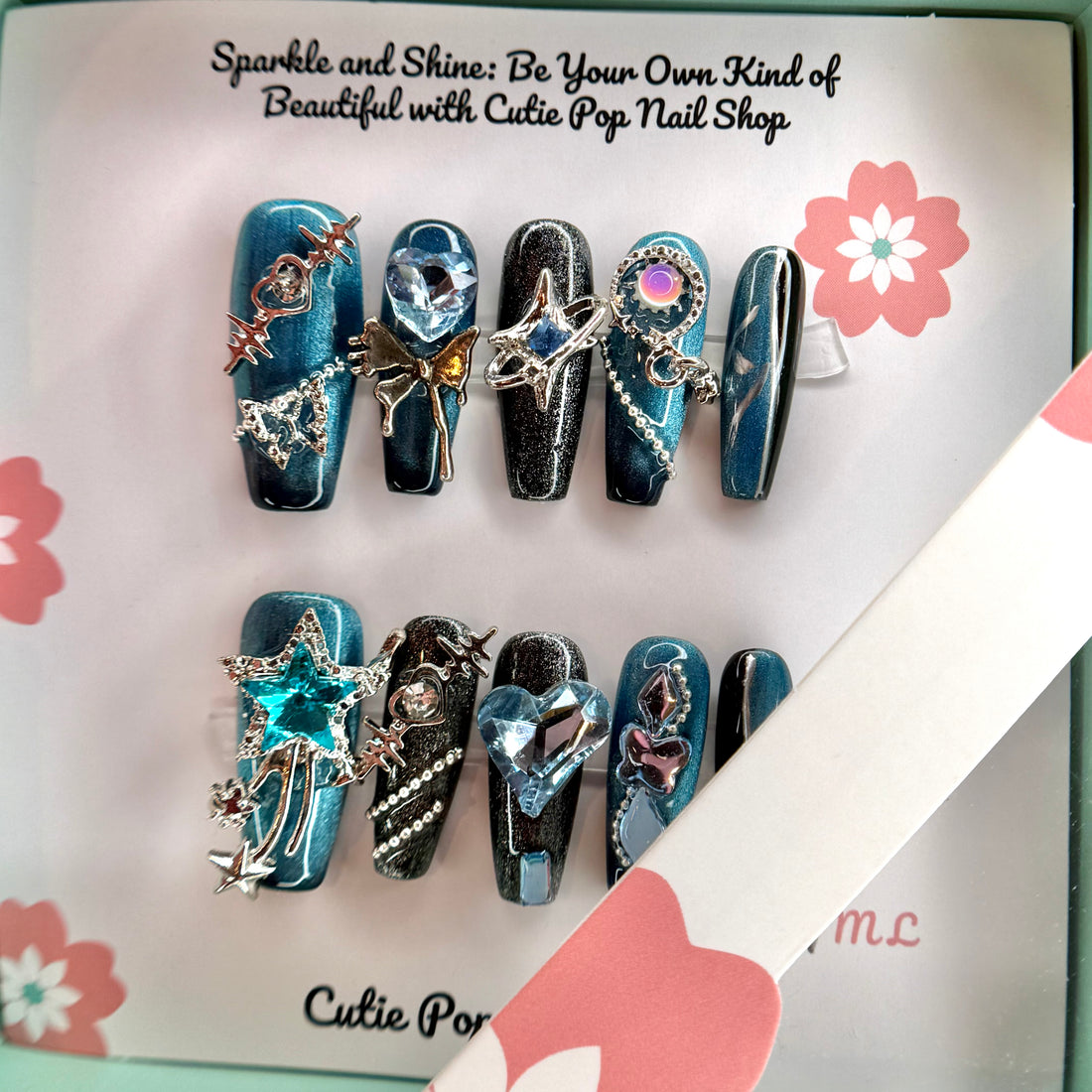 Y2K Teal Silver press on nails by CutiePop Nail Shop featuring medium coffin shaped nails in bold teal and silver tones with a chrome finish, heart and star accents, and a rock star-inspired Y2K aesthetic.

