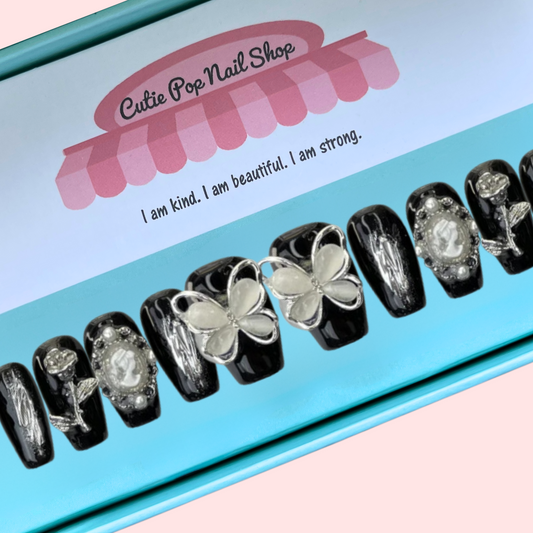 Black Butterfly press on nails by CutiePop Nail Shop featuring short length coffin shaped nails in a glossy jet black base. Several accent nails display clear backgrounds with bold black butterfly wing decals and metallic silver stud embellishments. Includes a full reusable kit: ten handmade nails, jelly adhesive tabs, mini nail file, and cuticle stick—offering a modern, edgy butterfly goth aesthetic.