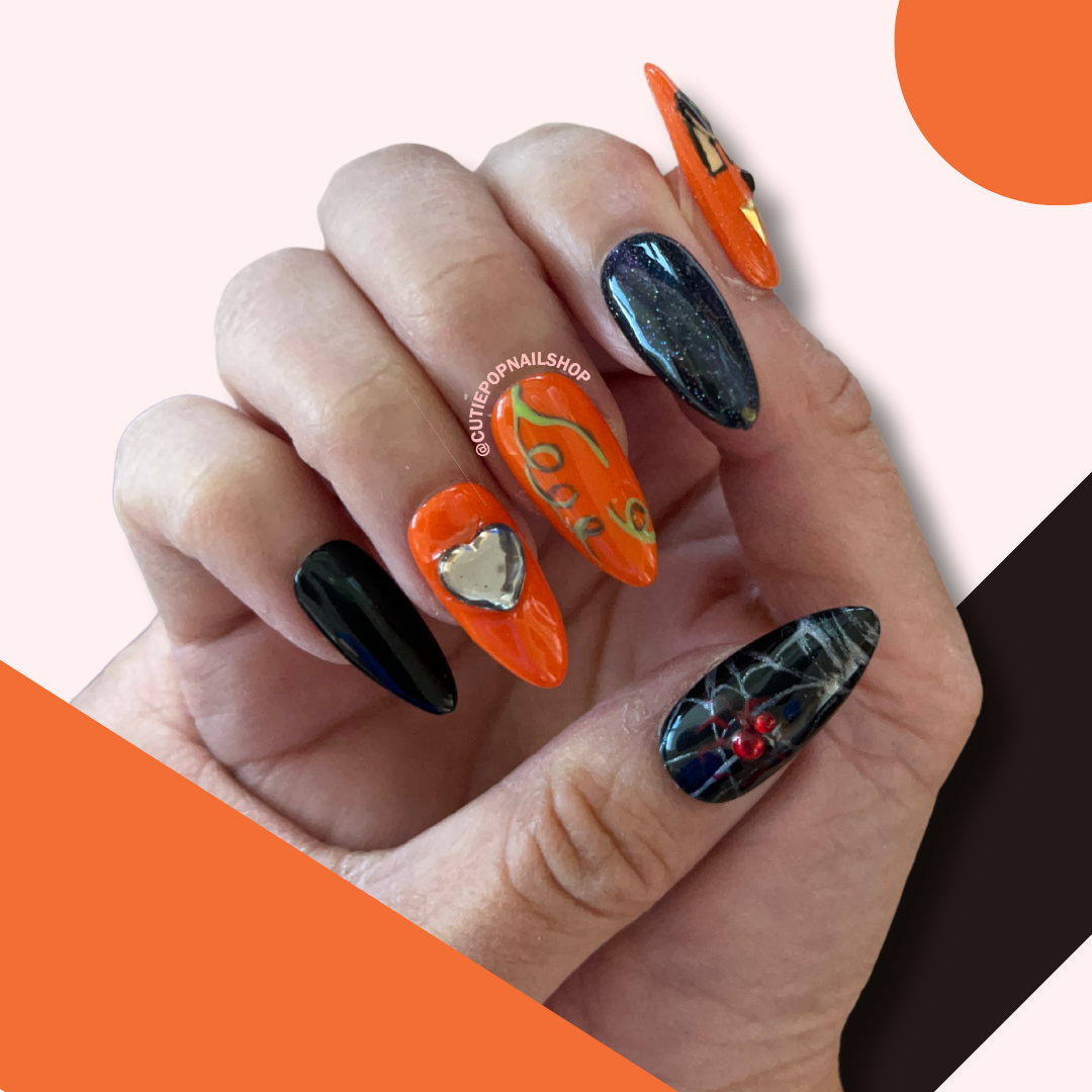 Pumpkin Cat Nails (Size SMALL) press‑on nails by CutiePop Nail Shop featuring medium-length almond-shaped nails in a vivid orange and deep black palette. These Halloween-themed nails showcase hand-drawn pumpkin faces with adorable black cats nestled inside their grinning mouths, accented by tiny spider motifs (one with a red rhinestone body), cat-eye polish finish, and a dainty heart charm. Comes as a complete reusable kit with ten handmade nails sized at 15‑11‑12‑11‑9.5 mm (thumb to pinky), plus adhesive t