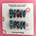 Y2K Teal Silver press on nails by CutiePop Nail Shop featuring medium coffin shaped nails in bold teal and silver tones with a chrome finish, heart and star accents, and a rock star-inspired Y2K aesthetic.


