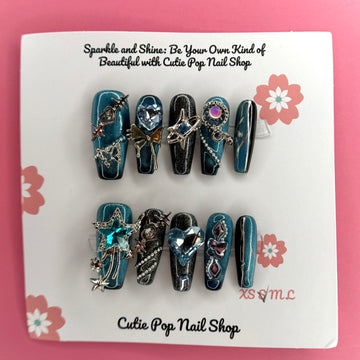 Y2K Teal Silver press on nails by CutiePop Nail Shop featuring medium coffin shaped nails in bold teal and silver tones with a chrome finish, heart and star accents, and a rock star-inspired Y2K aesthetic.

