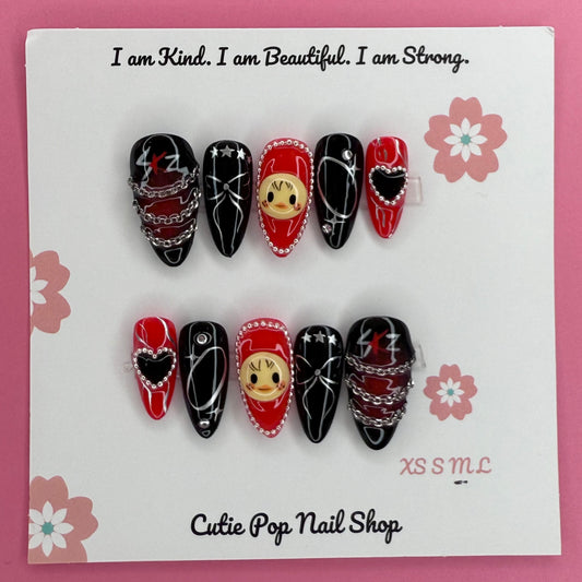 Stray Kids Concert-Inspired press on nails by CutiePop Nail Shop featuring medium almond shaped nails in bold red and black tones, adorned with heart charms, chains, and cartoon face accents. Designed for fans who want to rock a fierce, edgy look with playful K-pop flair.

