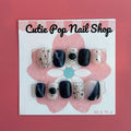 Abstract Gem press‑on nails by CutiePop Nail Shop featuring short-length squoval (square-oval) nails in a bold contrasting palette of glossy black and nude tones, accented by irregular abstract brush strokes and oversized metallic gemstone clusters. Includes reusable adhesive tabs, mini nail file, and a cuticle stick for full DIY application—delivering an edgy, artistic manicure with luxe shine.