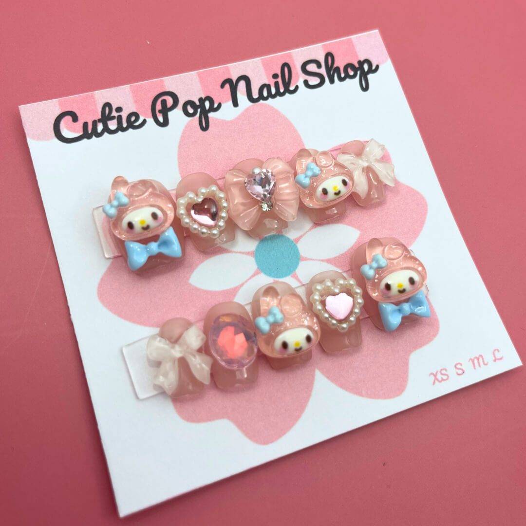 Bunny Pink Bow press on nails by CutiePop Nail Shop featuring short or medium coffin shaped nails in soft pink tones, adorned with adorable bunny motifs, dainty bow accents, and subtle glitter details. Designed for a sweet, playful look with a kawaii charm. Includes a full DIY kit with 10 reusable handmade nails, jelly adhesive tabs, a mini nail file, and a cuticle stick.


