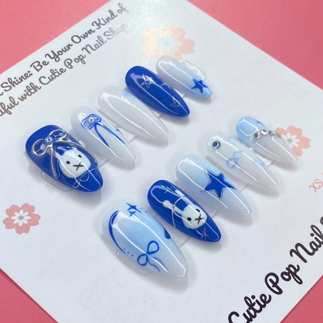 Bunny Starlight press‑on nails by CutiePop Nail Shop featuring a playful mix of glossy royal blue and clean white almond‑shaped nails, accented with hand-painted bunny motifs, delicate bow ribbons, and shimmering star charms—creating a whimsical, dreamy aesthetic perfect for kawaii-inspired looks.