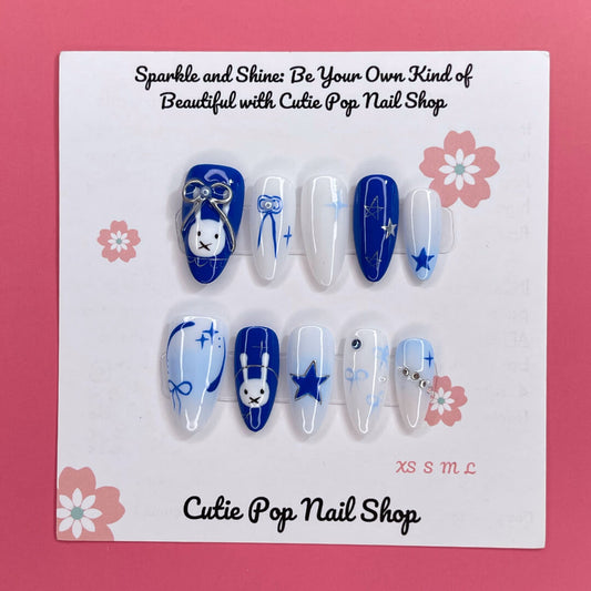 Bunny Starlight press‑on nails by CutiePop Nail Shop featuring a playful mix of glossy royal blue and clean white almond‑shaped nails, accented with hand-painted bunny motifs, delicate bow ribbons, and shimmering star charms—creating a whimsical, dreamy aesthetic perfect for kawaii-inspired looks.