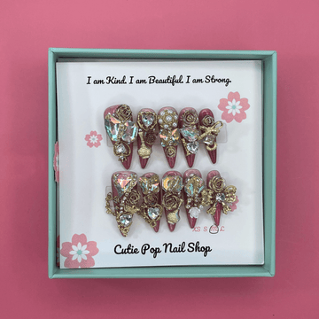 Bougie Bling 12 press on nails by CutiePop Nail Shop featuring long stiletto shaped nails with a glamorous deep dark burgundy or smoky wine toned glitter base. Lavish oversized 3D gem clusters in jewel tones such as ruby and crystal are complemented by sparkling rhinestones and metallic accents—arranged in an opulent, high impact luxury statement manicure.

