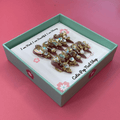 Bougie Bling 12 press on nails by CutiePop Nail Shop featuring long stiletto shaped nails with a glamorous deep dark burgundy or smoky wine toned glitter base. Lavish oversized 3D gem clusters in jewel tones such as ruby and crystal are complemented by sparkling rhinestones and metallic accents—arranged in an opulent, high impact luxury statement manicure.


