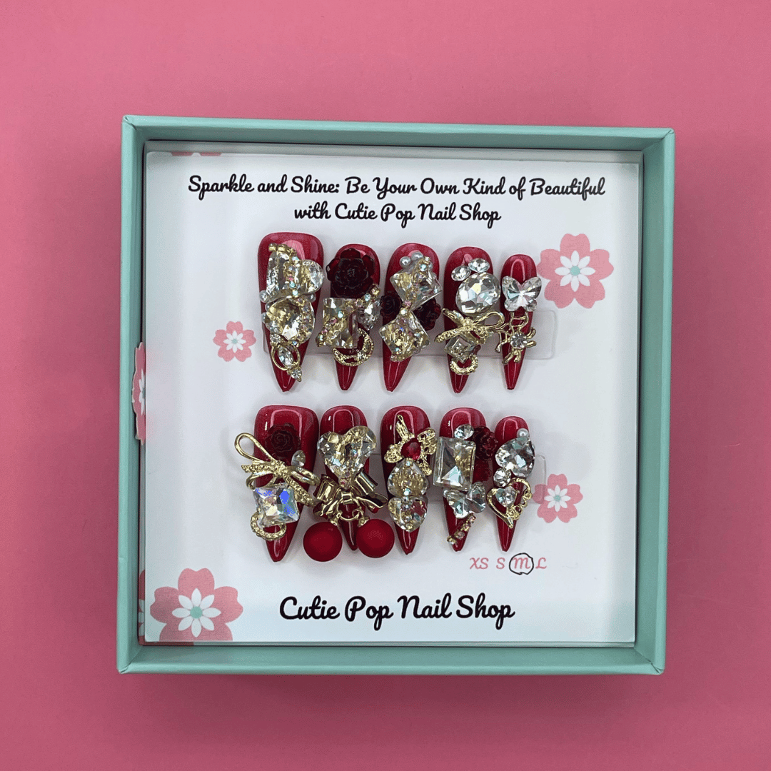 Bougie Bling 13 press on nails by CutiePop Nail Shop featuring long stiletto shaped nails with a rich deep burgundy red or wine toned glitter base. Lavish oversized 3D gem clusters in jewel tones including ruby and crystal are accentuated with sparkling rhinestones and metallic highlights for a dramatic, high end glitzy manicure.