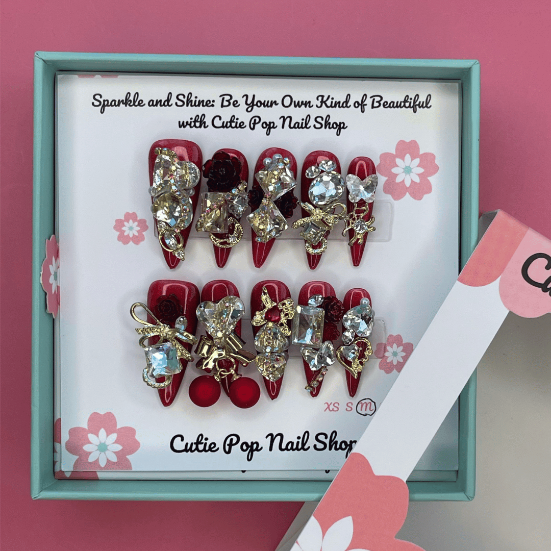 Bougie Bling 13 press on nails by CutiePop Nail Shop featuring long stiletto shaped nails with a rich deep burgundy red or wine toned glitter base. Lavish oversized 3D gem clusters in jewel tones including ruby and crystal are accentuated with sparkling rhinestones and metallic highlights for a dramatic, high end glitzy manicure.
