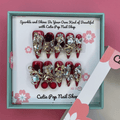 Bougie Bling 13 press on nails by CutiePop Nail Shop featuring long stiletto shaped nails with a rich deep burgundy red or wine toned glitter base. Lavish oversized 3D gem clusters in jewel tones including ruby and crystal are accentuated with sparkling rhinestones and metallic highlights for a dramatic, high end glitzy manicure.