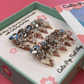 Bougie Bling 14 press on nails by CutiePop Nail Shop featuring long stiletto shaped nails with a dramatic glossy black base adorned with sparkling silver glitter accents and glamorous oversized 3D gem clusters in clear, smoke, and metallic tones, meticulously arranged for a bold, luxurious statement manicure.