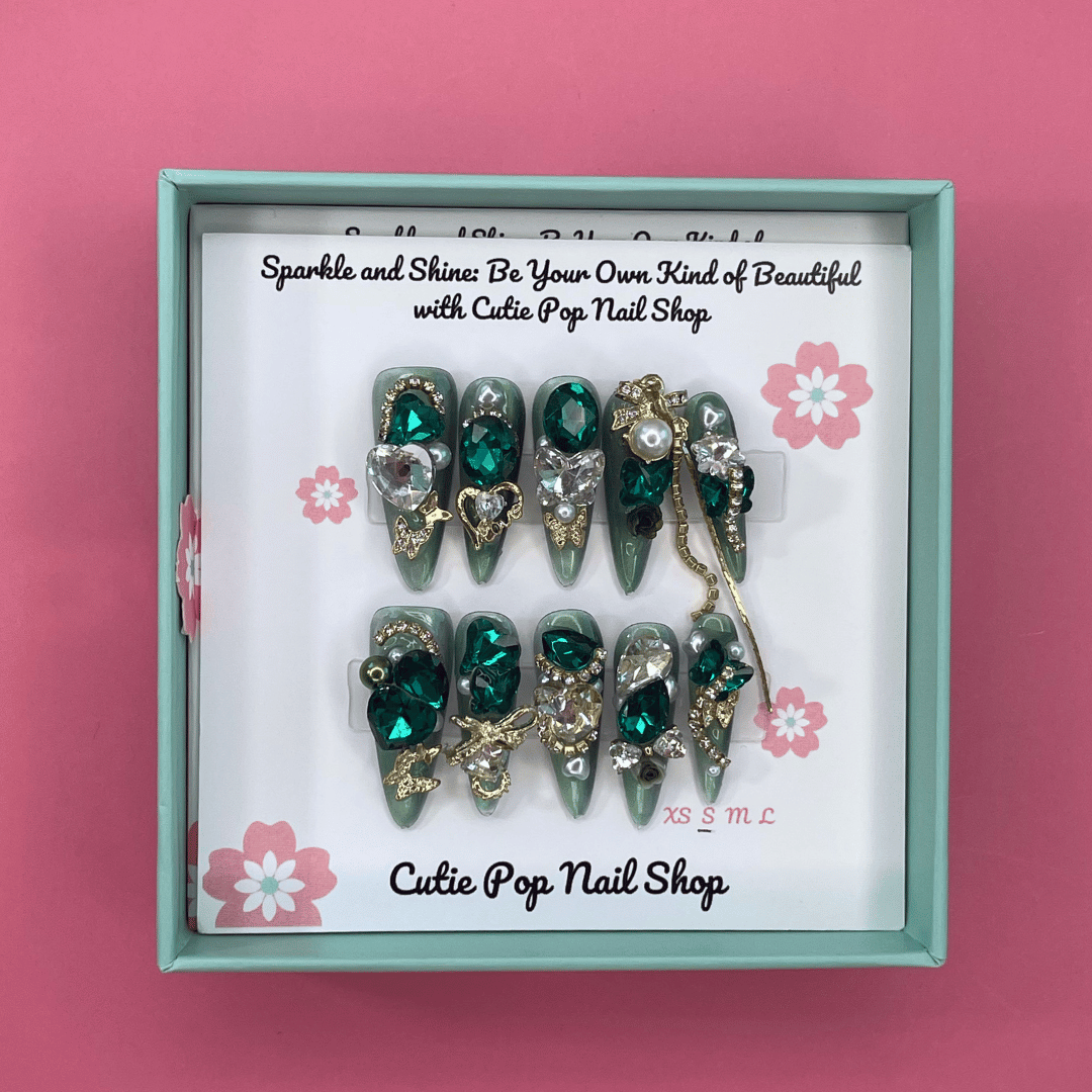 Bougie Bling 15 press on nails by CutiePop Nail Shop showcasing long coffin shaped nails with a dramatic glittery black base embellished with oversized 3D gem clusters in jewel tones, delicate rhinestone accents, and metallic detailing—all arranged in an ornate, high-impact luxury statement manicure.